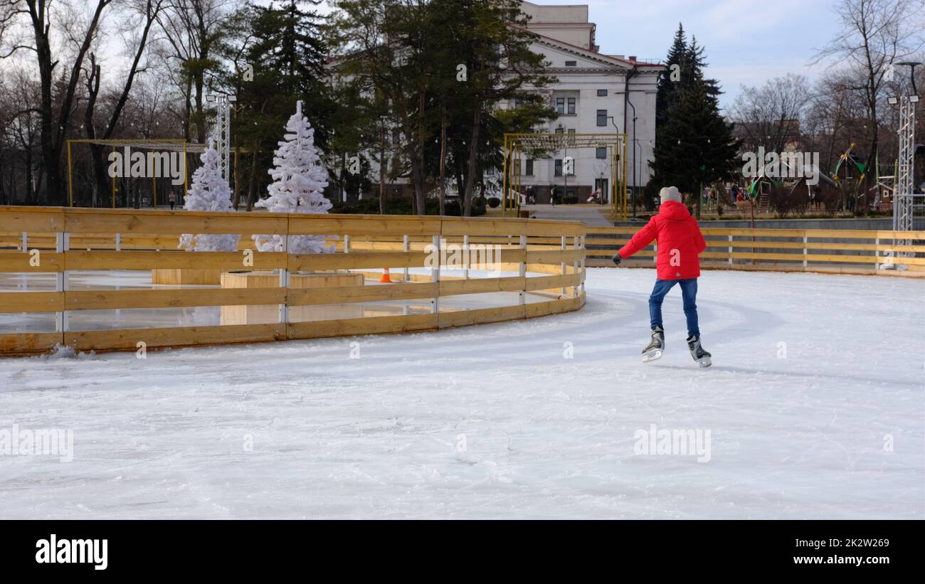 Ein Junge mit roter Jacke, tagsüber Schlittschuhlaufen, Spaß haben und auf der Eisbahn lernen Stockfoto