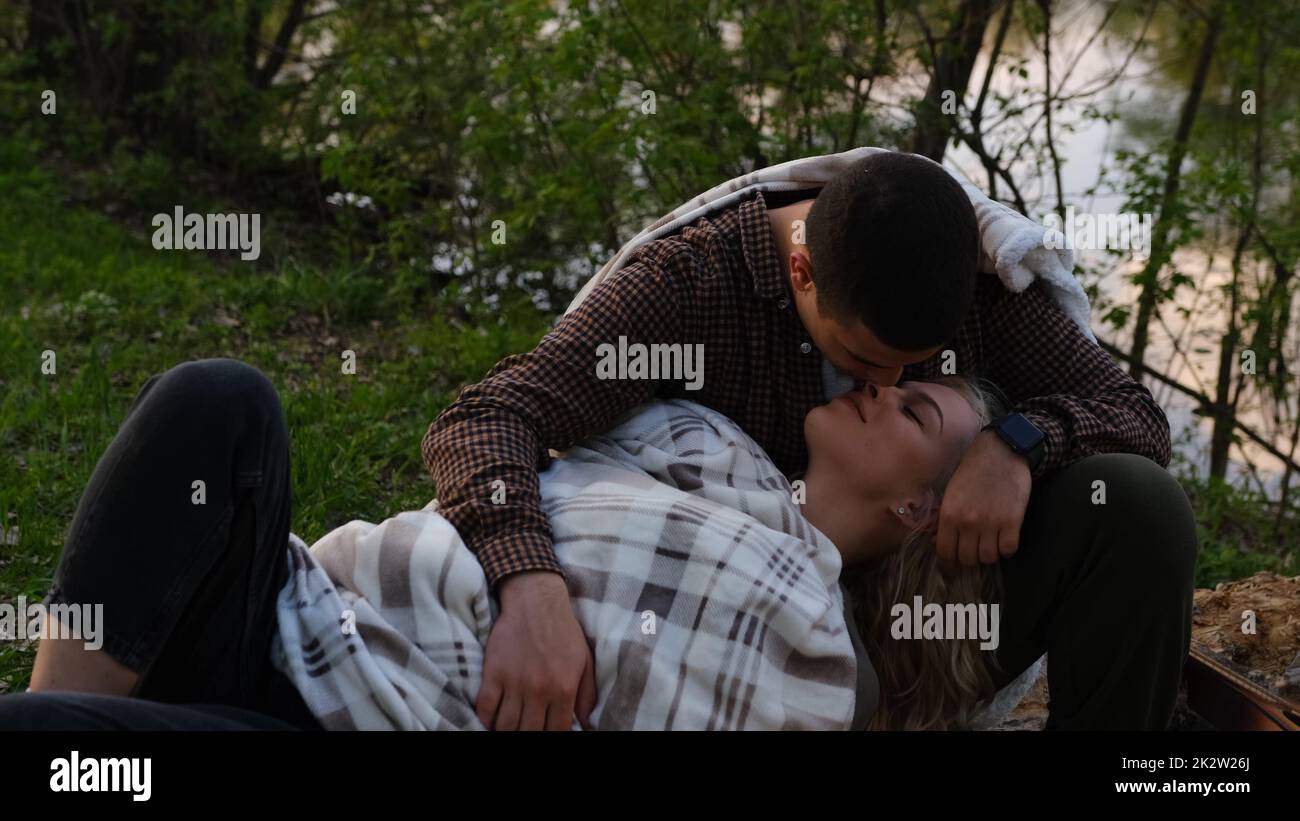 Ein attraktives Paar, das sich an einem sonnigen Tag im Wald entspannt, ein Mann, der seine Freundin küsst und in den Knien liegt. Camping-Liebesgeschichte Stockfoto
