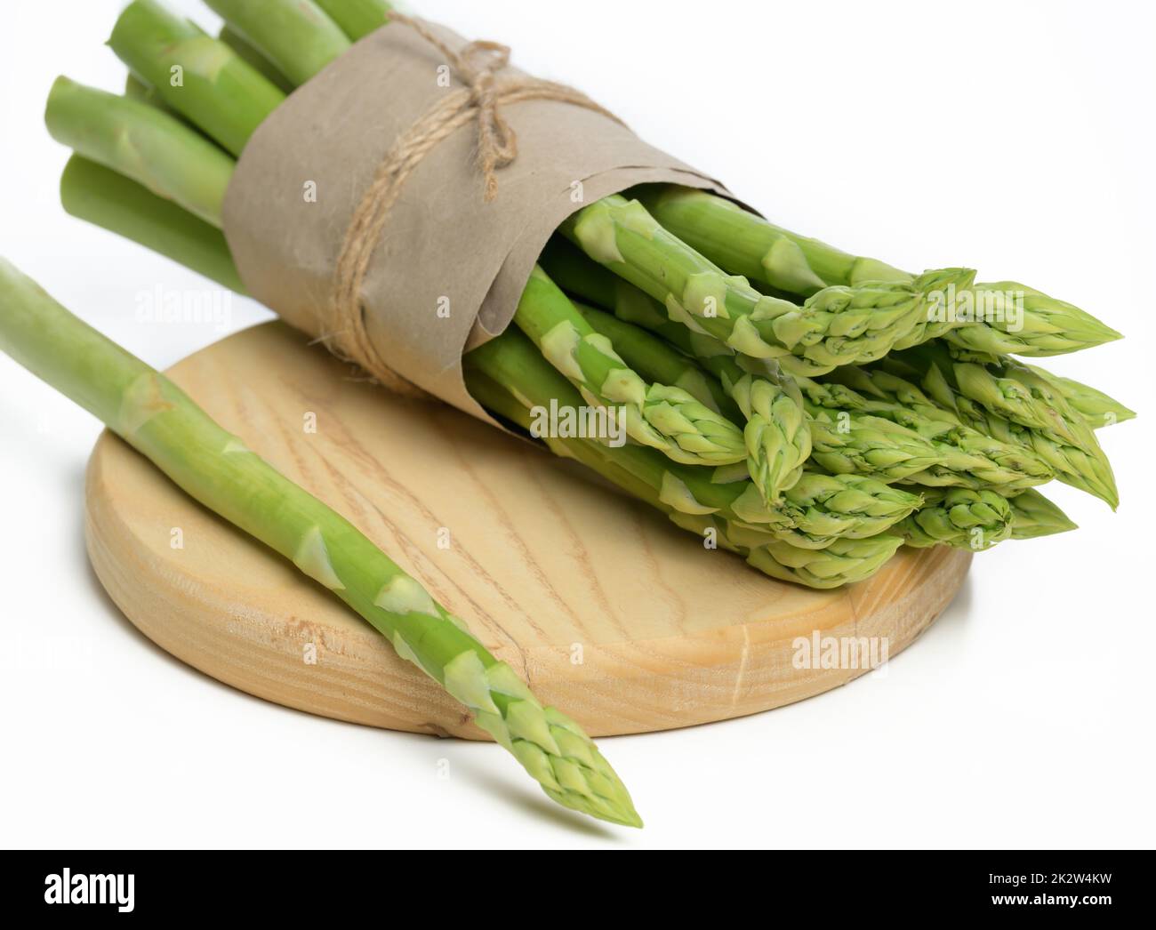 Ein paar frische Spargel, eingewickelt in braunem Papier, liegt auf einem Holzteller Stockfoto