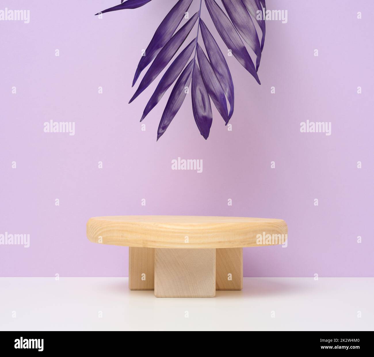 Bühne für die Präsentation von Produkten, Kosmetik mit einem runden Holzpodium und einem Palmblatt. Violetter Papierhintergrund Stockfoto