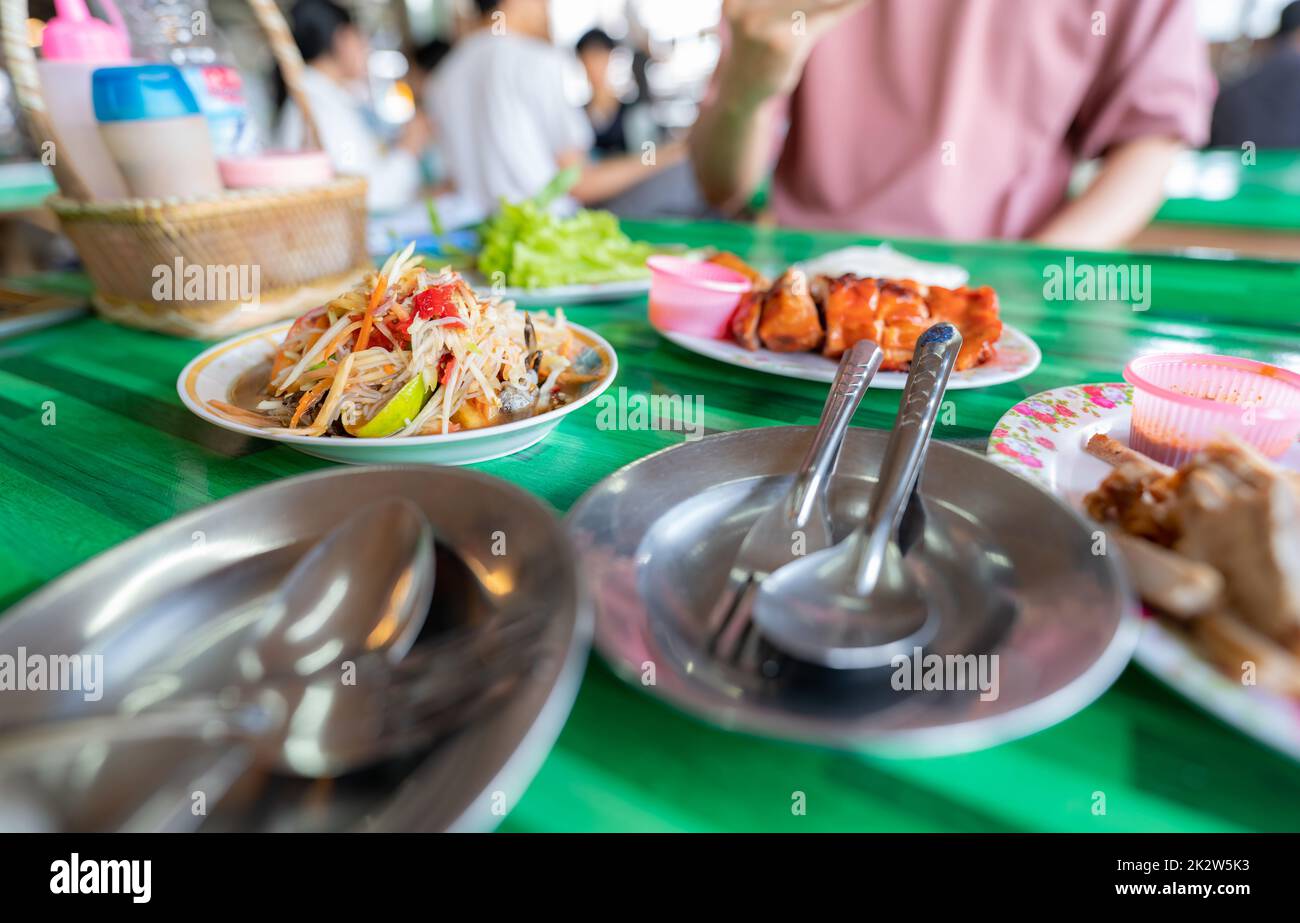 Würziger grüner Papayasalat oder Som TUM mit thailändischen Reisnudeln. Street Food mit heißem und würzigem Gericht in Thailand. Das berühmte lokale thailändische Street Food. Thailändische Esarn-Küche. Papayasalat mit gegrilltem Hähnchen. Stockfoto