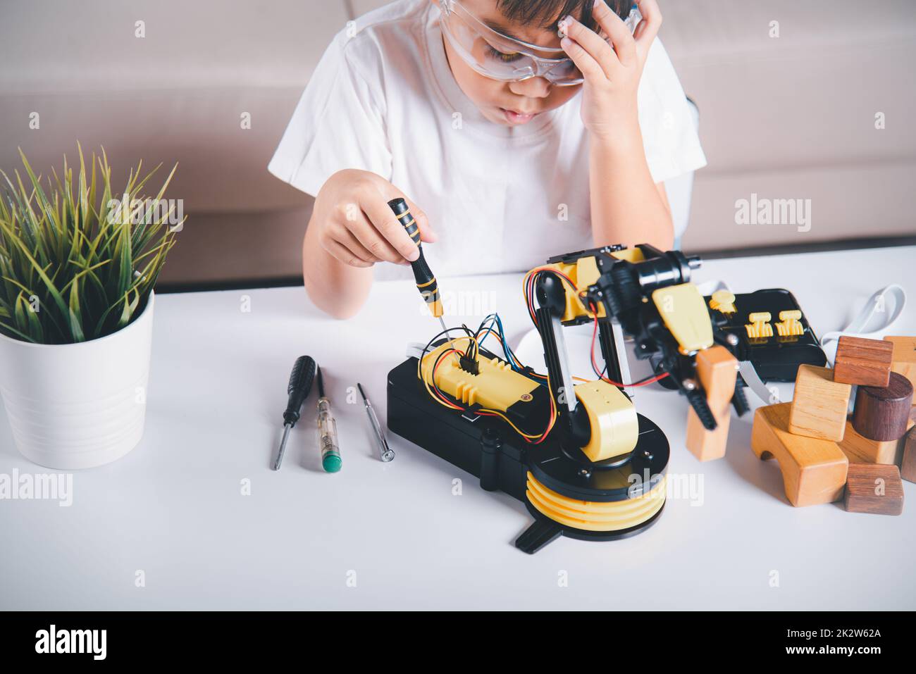 Ein glücklicher asiatischer kleiner Junge, der mit einem Schraubenzieher Schrauben am Roboterarm in der Hauswerkstatt repariert Stockfoto