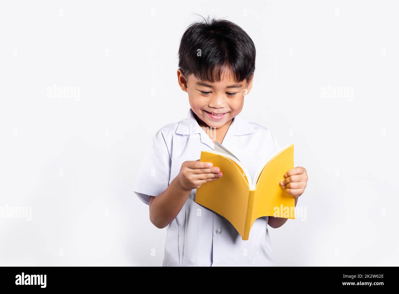 Asiatisches Kleinkind lächelt glücklich und trägt Thai-Uniform, rote Hosen, die stehen und ein Buch lesen Stockfoto