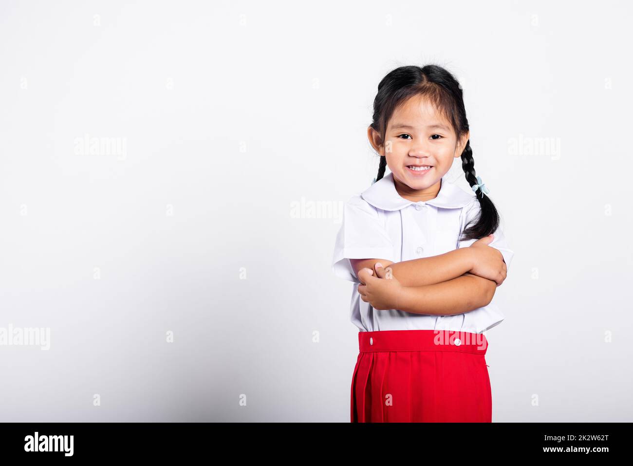 Asiatisches Kleinkind lächelt fröhlich und trägt Thai-Uniform als Studentin, roter Rock mit zusammengeklappten Armen Stockfoto