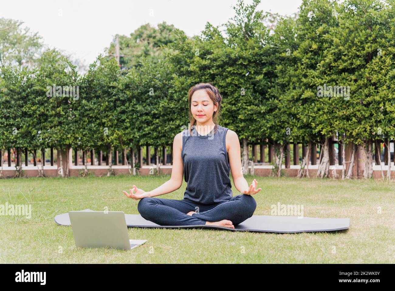 Frau, die während eines Online-Videotrainings mit einem Laptop Yoga im Freien praktiziert Stockfoto