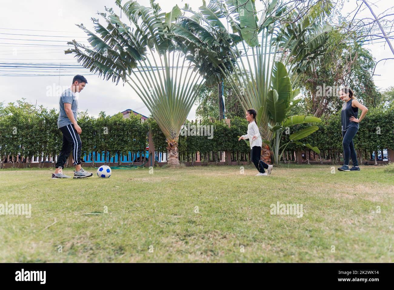 Mutter, Vater und Tochter spielen Fußball in der Natur, einem Gartenpark Stockfoto