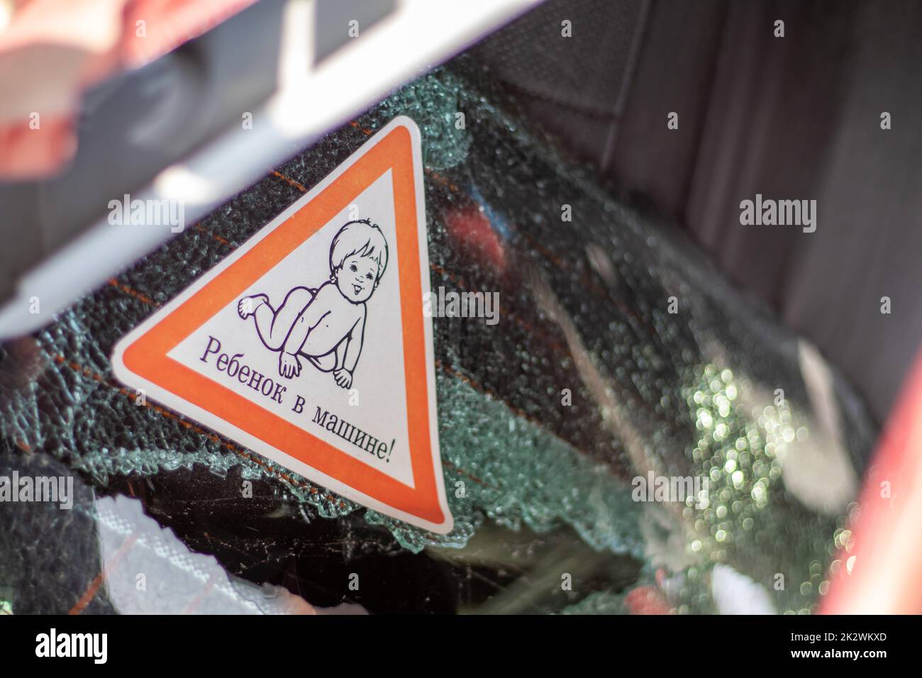 Warnzeichen von Kindern im Auto nach einem Unfall mit blutigem Glasbruch. Übersetzung: Kind im Auto. Nahaufnahme eines weißen Babyaufklebers an der Rückseite des Fahrzeugs. Stockfoto