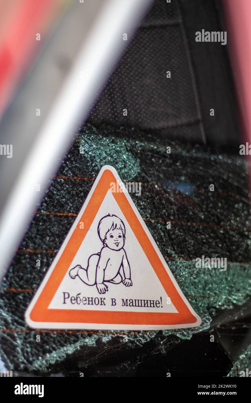 Warnzeichen von Kindern im Auto nach einem Unfall mit blutigem Glasbruch. Übersetzung: Kind im Auto. Nahaufnahme eines weißen Babyaufklebers an der Rückseite des Fahrzeugs. Vertikales Foto. Stockfoto