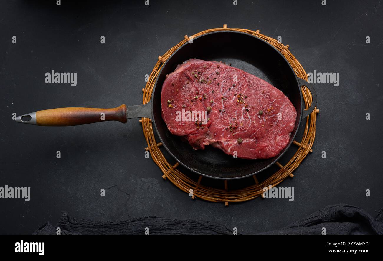 Rohes Rinderfilet liegt in einer runden Metallpfanne auf einem schwarzen Tisch Stockfoto