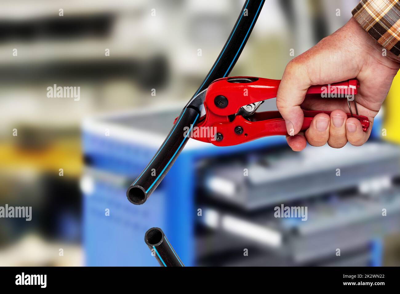 Handwerker-Werkzeuge. Ein Mann schneidet ein Stück PE-Druckrohr oder Wasserrohr mit einem roten pvc-Rohrabschneider über abstrakten industriellen Hintergrund. Trink- und Versorgungswassersysteme. Stockfoto