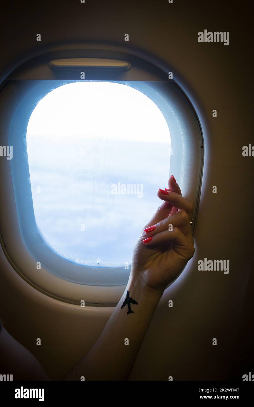 Schöne Aussicht vom Flugzeugfenster auf die Luftwolken, Hand eines Mädchens mit Tätowierung Stockfoto