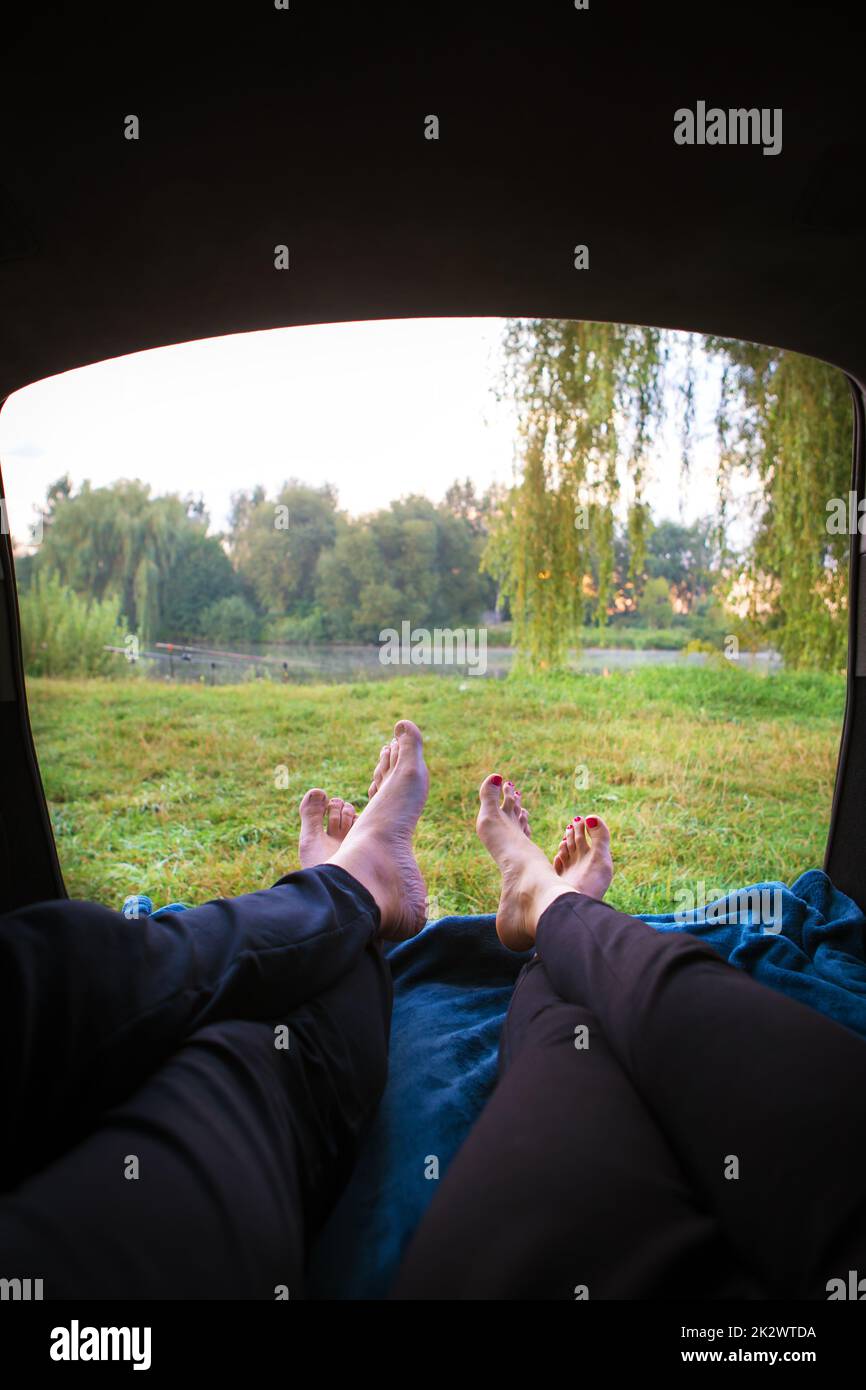 Mann und Frau entspannen sich im Kofferraum eines Autos in der Nähe eines Sees Stockfoto