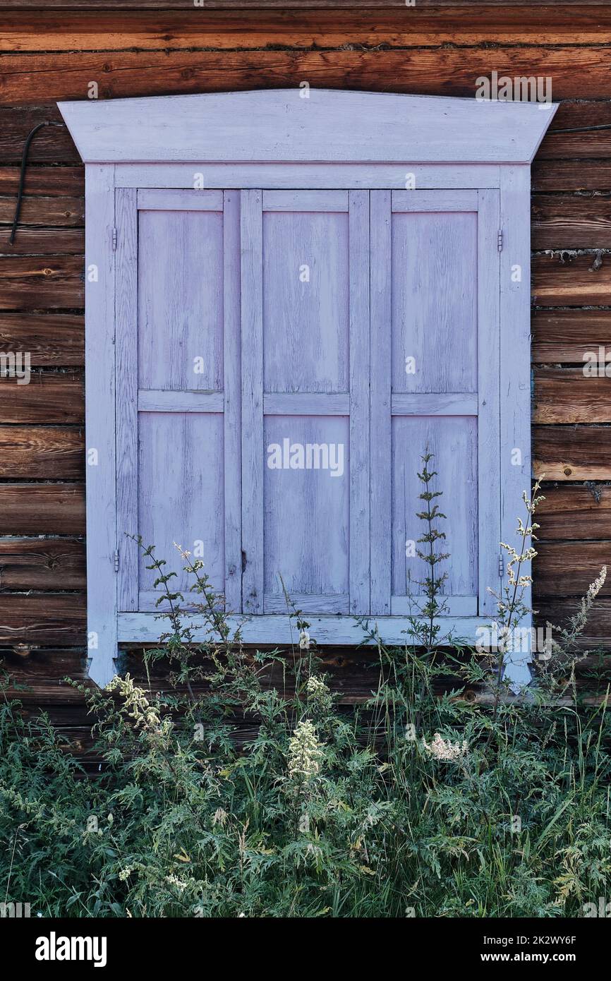 Altes Holzfenster mit geschlossenen schäbigen Fensterläden in Lavendelfarbe. Fassade des typischen ländlichen Holzhauses, Russland Stockfoto