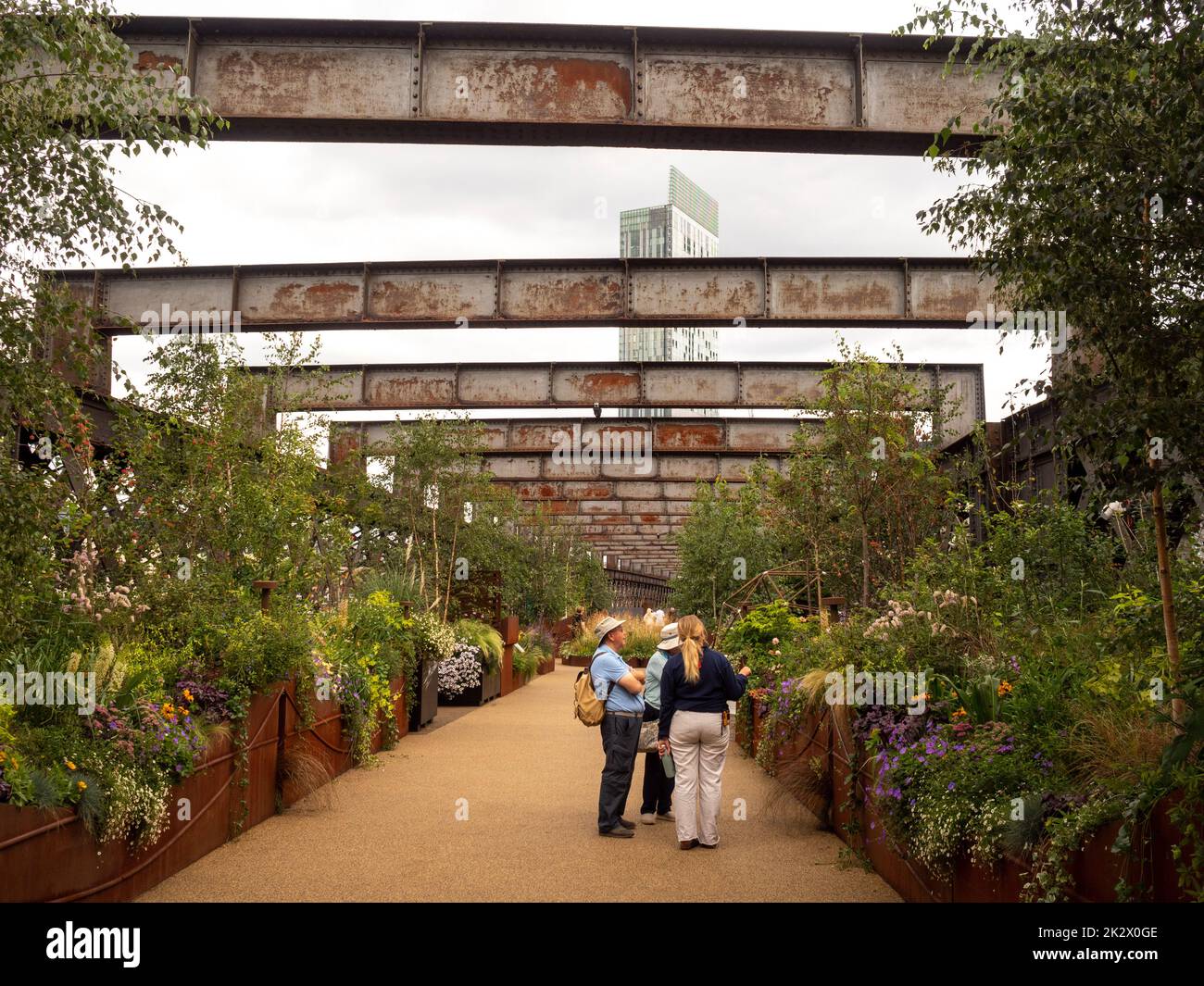 Besucher, die die erhöhten Blumenbeete des Sky Garden auf dem Castlefield Viaduct mit dem Beetham Tower in der Ferne bestaunen. Manchester. Stockfoto