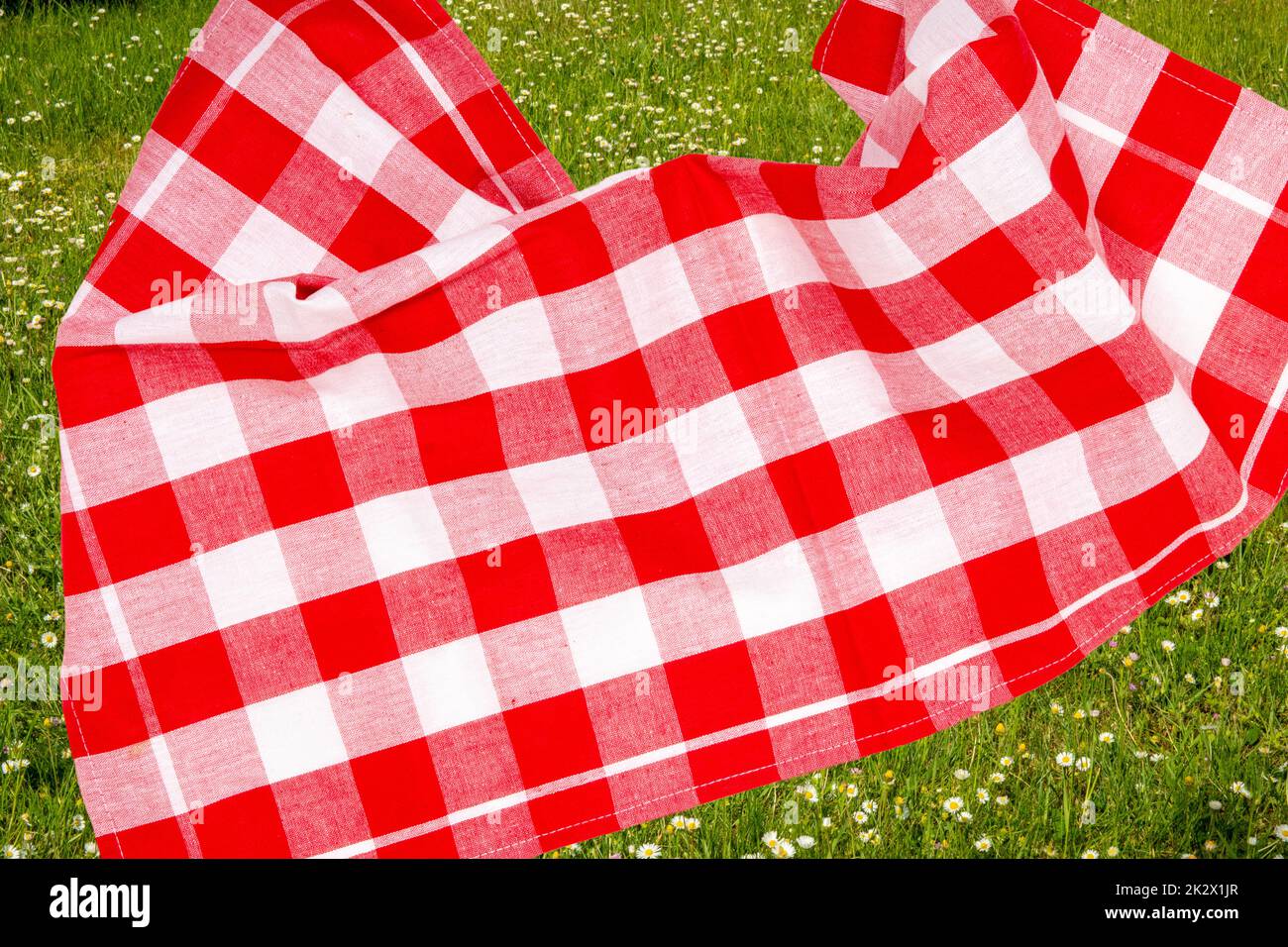 Picknick-Hintergrund. Rotes kariertes Picknicktuch auf verschwommenem, sonnenüberflutetem, üppigem Gras mit Schwerpunkt auf Serviette. Schöner Hintergrund für die Produktplatzierung oder -Montage. Stockfoto