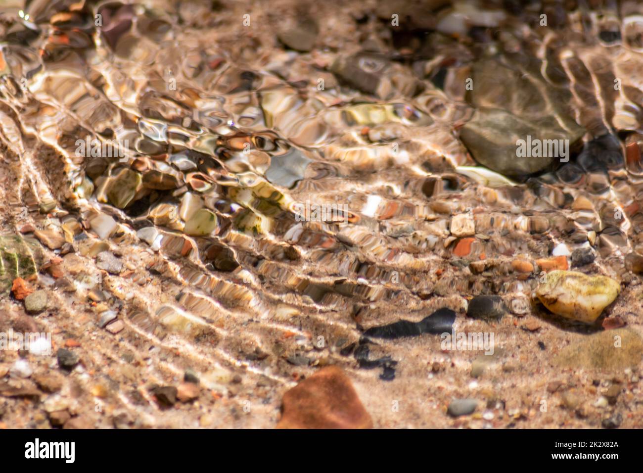 Steine im glitzernden Wasser mit sonnigen Reflexionen im Wasser eines kristallklaren Wasserbaches, während der idyllische natürliche Hintergrund Zen-Meditation, kleine Wellen und seidige Wellen in einer gesunden Bergquelle zeigt Stockfoto