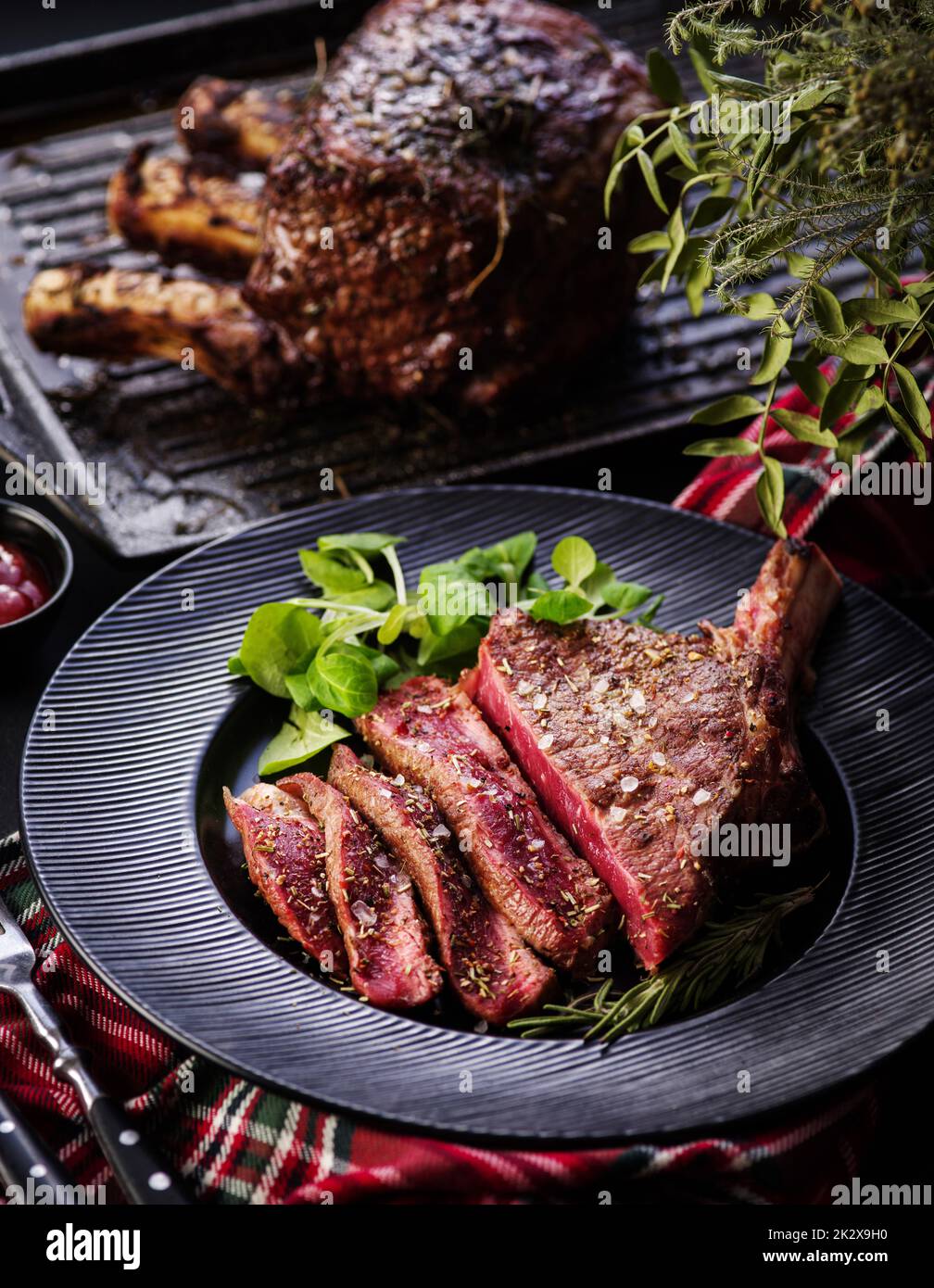 Steak auf den Knochen. Rib-Eye. Tomahawk Steak auf dem schwarzen Teller mit Rosmarin. Rösten - Selten. Entrecote Stockfoto