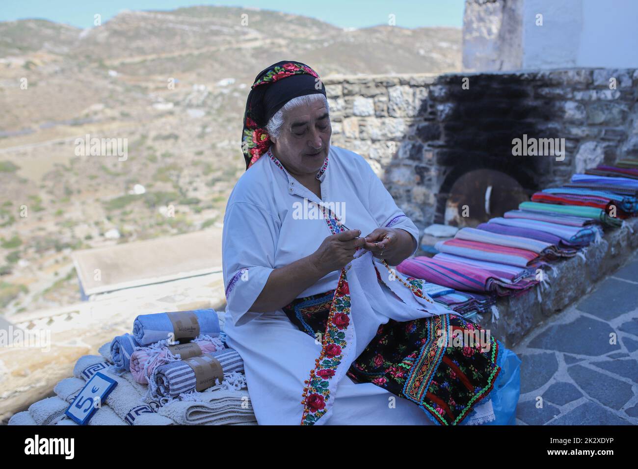 Karpathos, Griechenland. 10. August 2021. Frau Rigopoula außerhalb ihres Ladens mit lokalen handgewebten Textilien, traditionellen Schals und traditionellen Mini-Kostümen für Puppen, Olympos Dorf, Karpathos Insel. Karpathos ist die zweitgrößte Insel des griechischen dodekanischen Inselkomplexes in der südöstlichen Ägäis. Die Insel Karpathos hat immer noch ihre traditionelle Lebensweise, wie das Dorf Olympos, wo die Einheimischen noch immer die traditionellen Kostüme tragen. (Foto von Maria Makraki/SOPA Images/Sipa USA) Quelle: SIPA USA/Alamy Live News Stockfoto