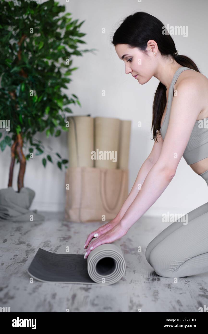 Eine junge, schöne Frau rollt eine Matte für Yoga oder Meditation auf. Stockfoto