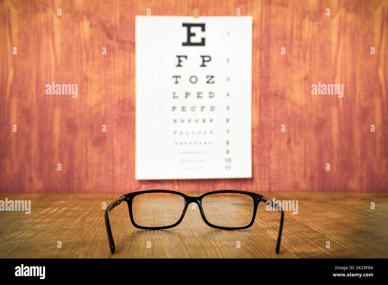 Brille auf Holztisch gegen Augenprüftafel Stockfoto