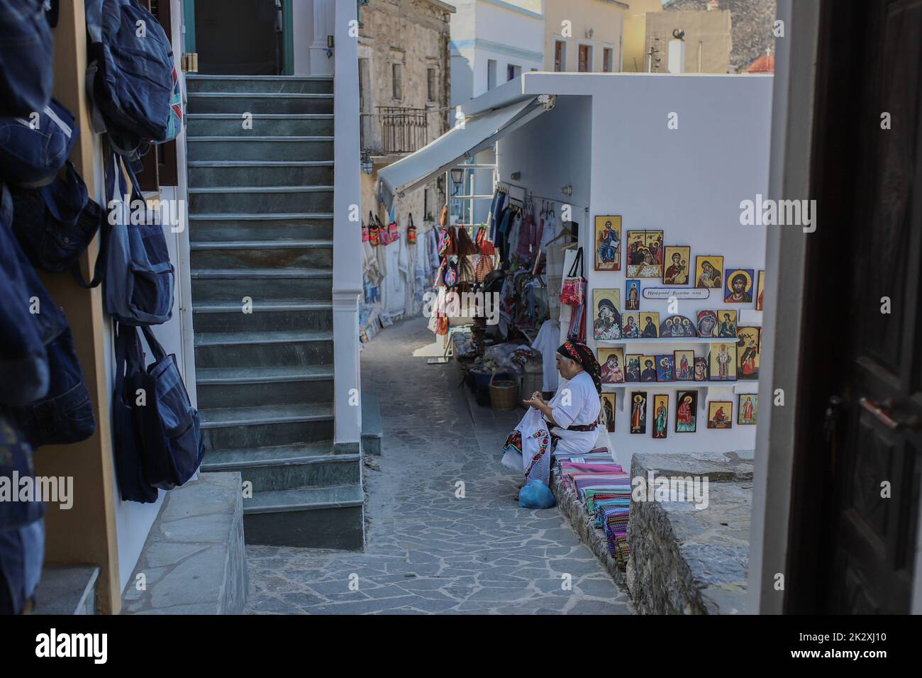 Karpathos, Griechenland. 10. August 2021. Frau Rigopoula außerhalb ihres Ladens mit lokalen handgewebten Textilien, traditionellen Schals und traditionellen Mini-Kostümen für Puppen, Olympos Dorf, Karpathos Insel. Karpathos ist die zweitgrößte Insel des griechischen dodekanischen Inselkomplexes in der südöstlichen Ägäis. Die Insel Karpathos hat immer noch ihre traditionelle Lebensweise, wie das Dorf 'Olympos', wo die Einheimischen immer noch die traditionellen Kostüme tragen. (Bild: © Maria Makraki/SOPA Images via ZUMA Press Wire) Stockfoto