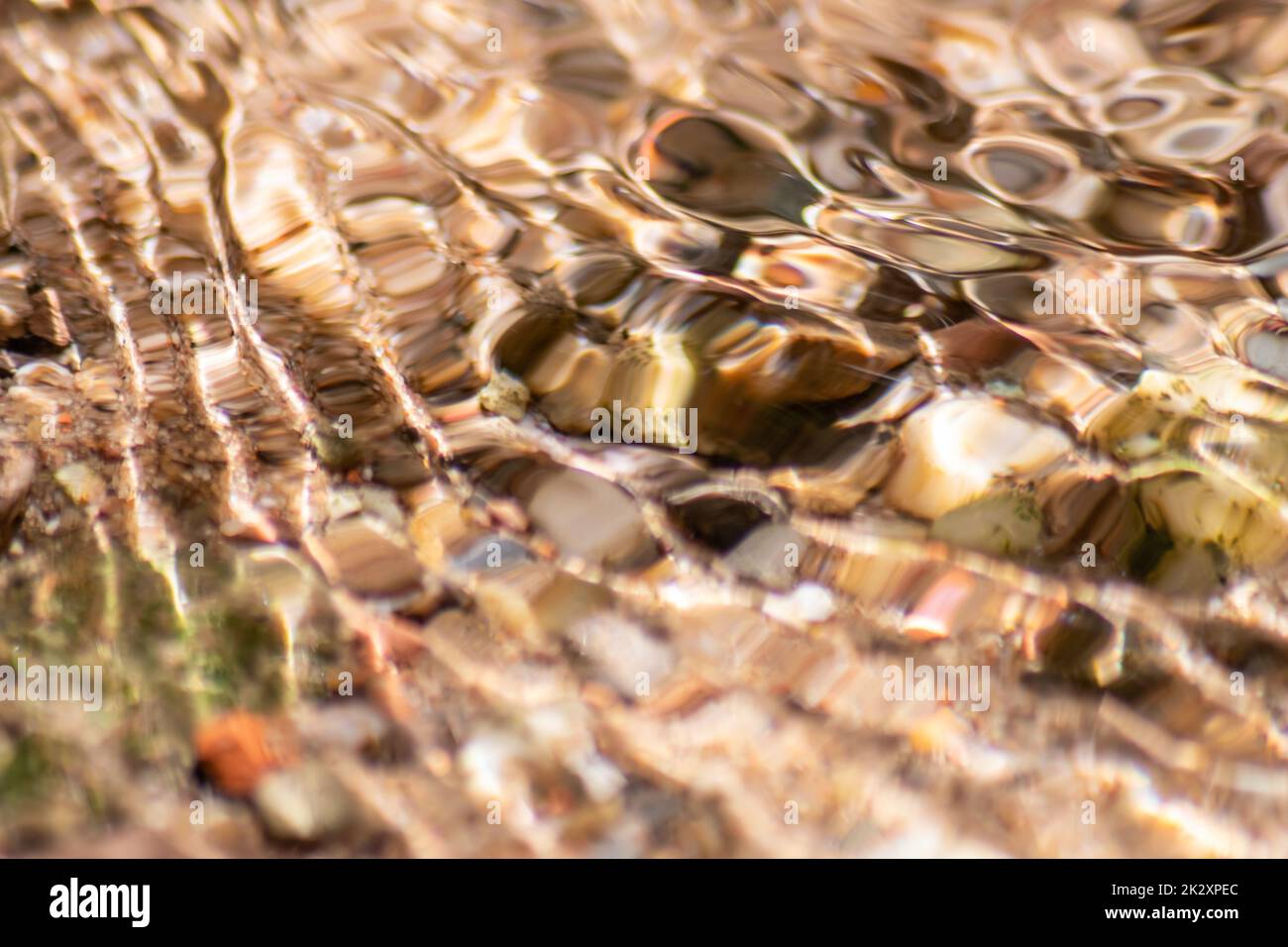 Steine im glitzernden Wasser mit sonnigen Reflexionen im Wasser eines kristallklaren Wasserbaches, während der idyllische natürliche Hintergrund Zen-Meditation, kleine Wellen und seidige Wellen in einer gesunden Bergquelle zeigt Stockfoto