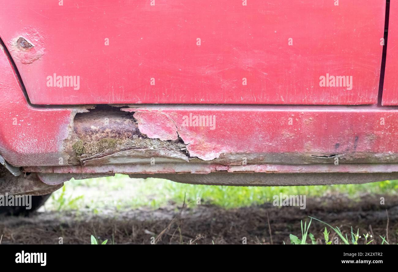 Rostige Fahrertürschweller. Korrosion der Karosserie eines roten alten Wagens nach Winter. Der Einfluss von Reagenzien im Winter auf eine ungeschützte Fahrzeugkarosserie. Schaden an der linken Seite, verdorbener Schwellwert unten. Stockfoto