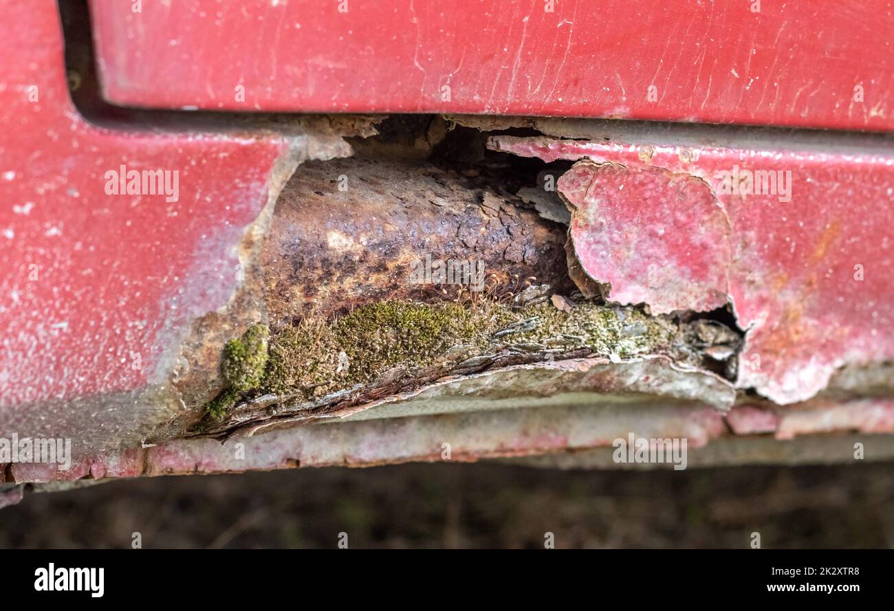 Rostige Fahrertürschweller. Korrosion der Karosserie eines roten alten Wagens nach Winter. Der Einfluss von Reagenzien im Winter auf eine ungeschützte Fahrzeugkarosserie. Schaden an der linken Seite, verdorbener Schwellwert unten. Stockfoto