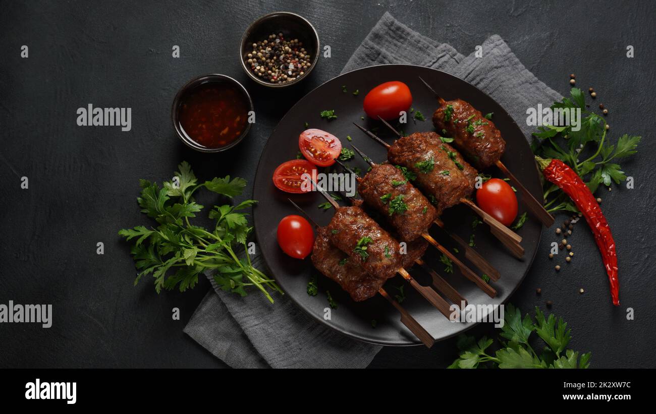 Shish Kebab ist eine beliebte Mahlzeit aus Spieß- und gegrillten Fleischwürfeln. Gerösteter Rinderkebab auf einem Holzspieß mit Gewürzen, Kräutern und Tomaten Stockfoto