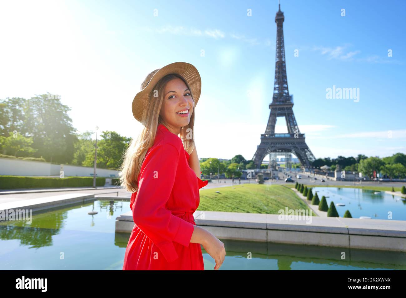 Urlaub in Paris. Elegante Dame in rotem Kleid und Hut lächelt vor der Kamera mit Eiffelturm im Hintergrund. Stockfoto