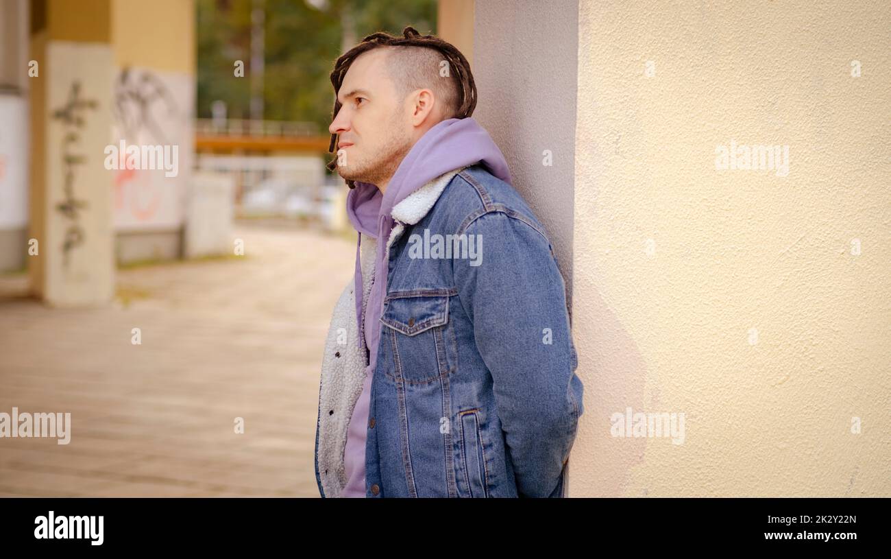 Porträt eines jungen, gutaussehenden Mannes mit Dreadlocks, die auf der Straße posieren, stehen und sich an einer Wand lehnen Stockfoto