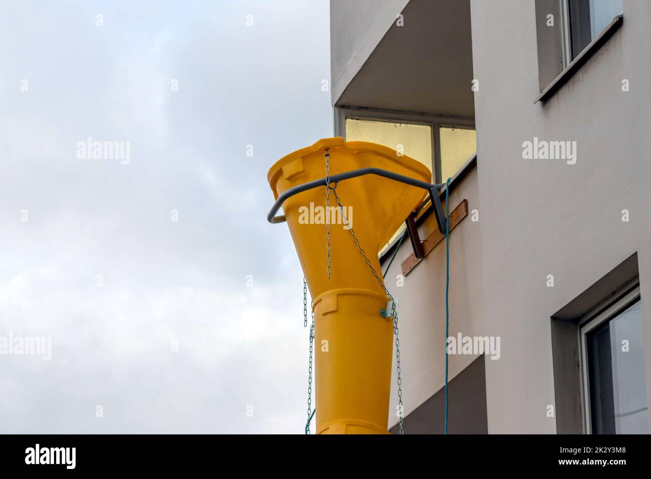Die gelbe Schutsche oder die Rutsche an der Fassade des alten weißen Hauses hilft bei der Renovierung und Renovierung des alten Gebäudes für die saubere Beseitigung von Schutt und die Abfallentsorgung in den Container für die Baustelle Stockfoto