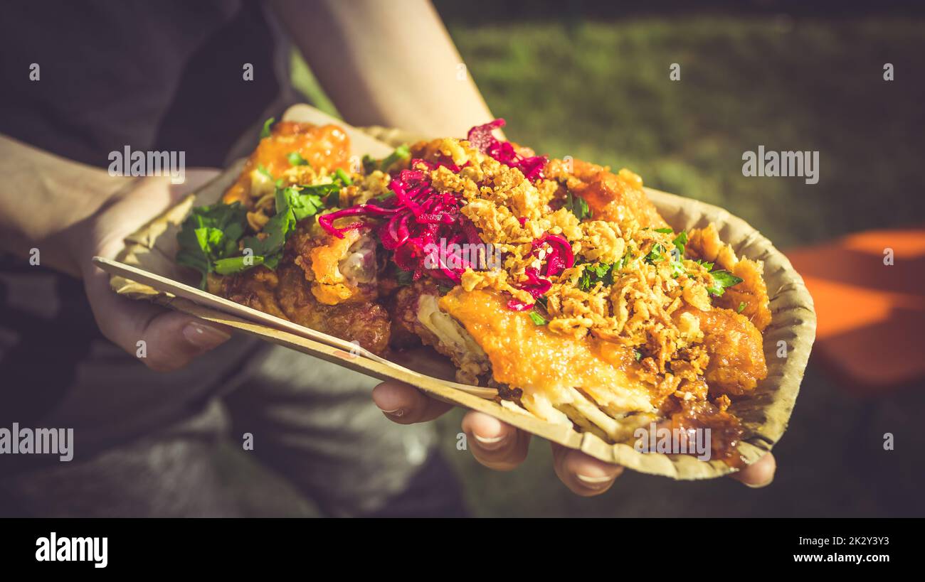 Street Food - Hand hält eine Portion würziger Hähnchenflügel mit Rotkohl und Kräutern Stockfoto