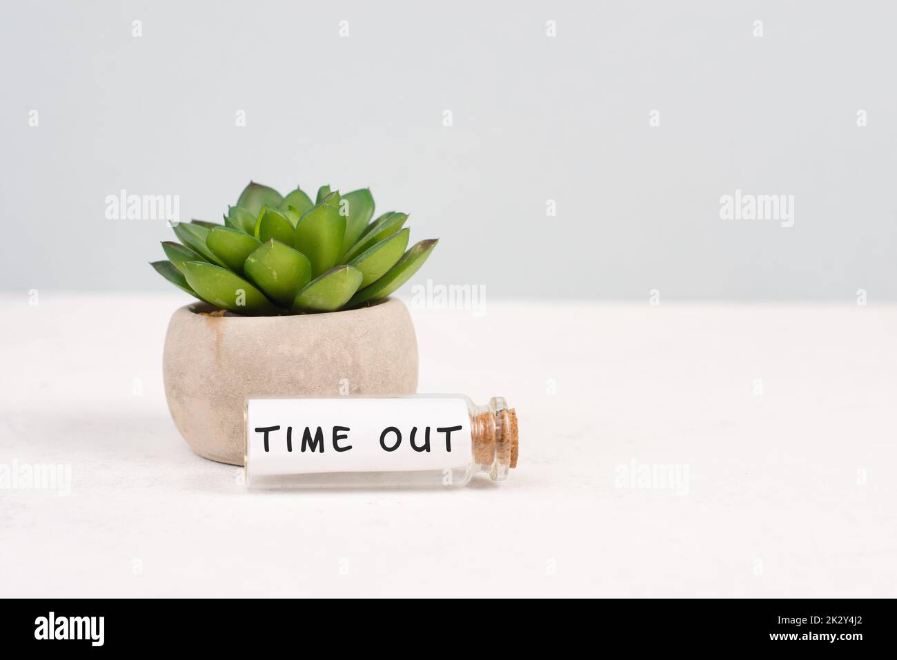 Kaktus in einem Topf auf grauem Hintergrund, Glasflasche mit dem Ausdruck Auszeit, Work-Life-Balance, Schreibtisch im Büro Stockfoto