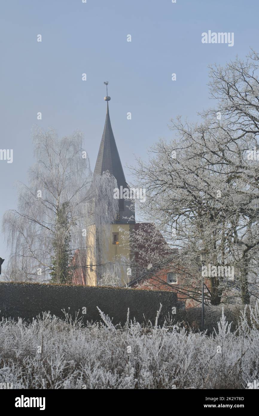 Deutsche Kirche in einer Winterwunderlandlandschaft mit Reif auf dem Kirchturm und einem großen Baum Stockfoto