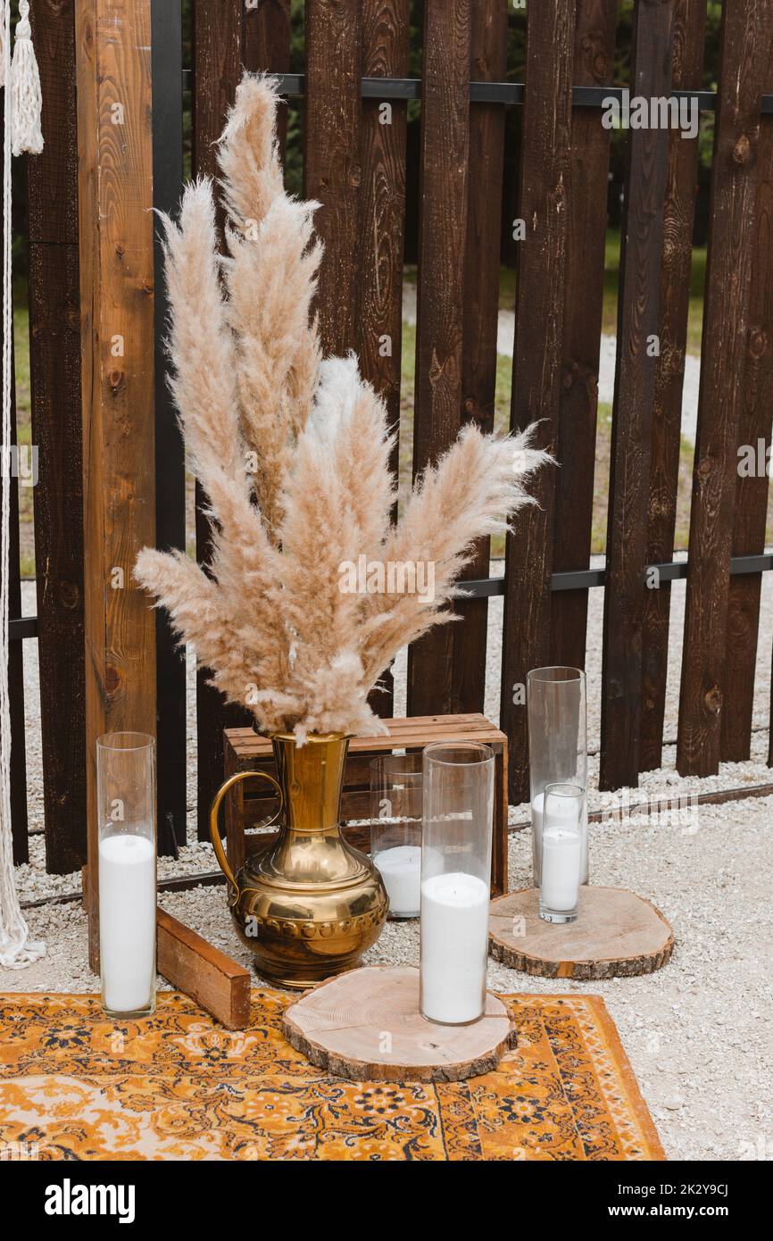 Hohe Pampa Gras in einer Vase und Kerzen in Glasbirnen gegen einen Holzzaun in Dekoration Party. Pampas Gras im Innenraum, Boho-Stil. Dekor für Stockfoto