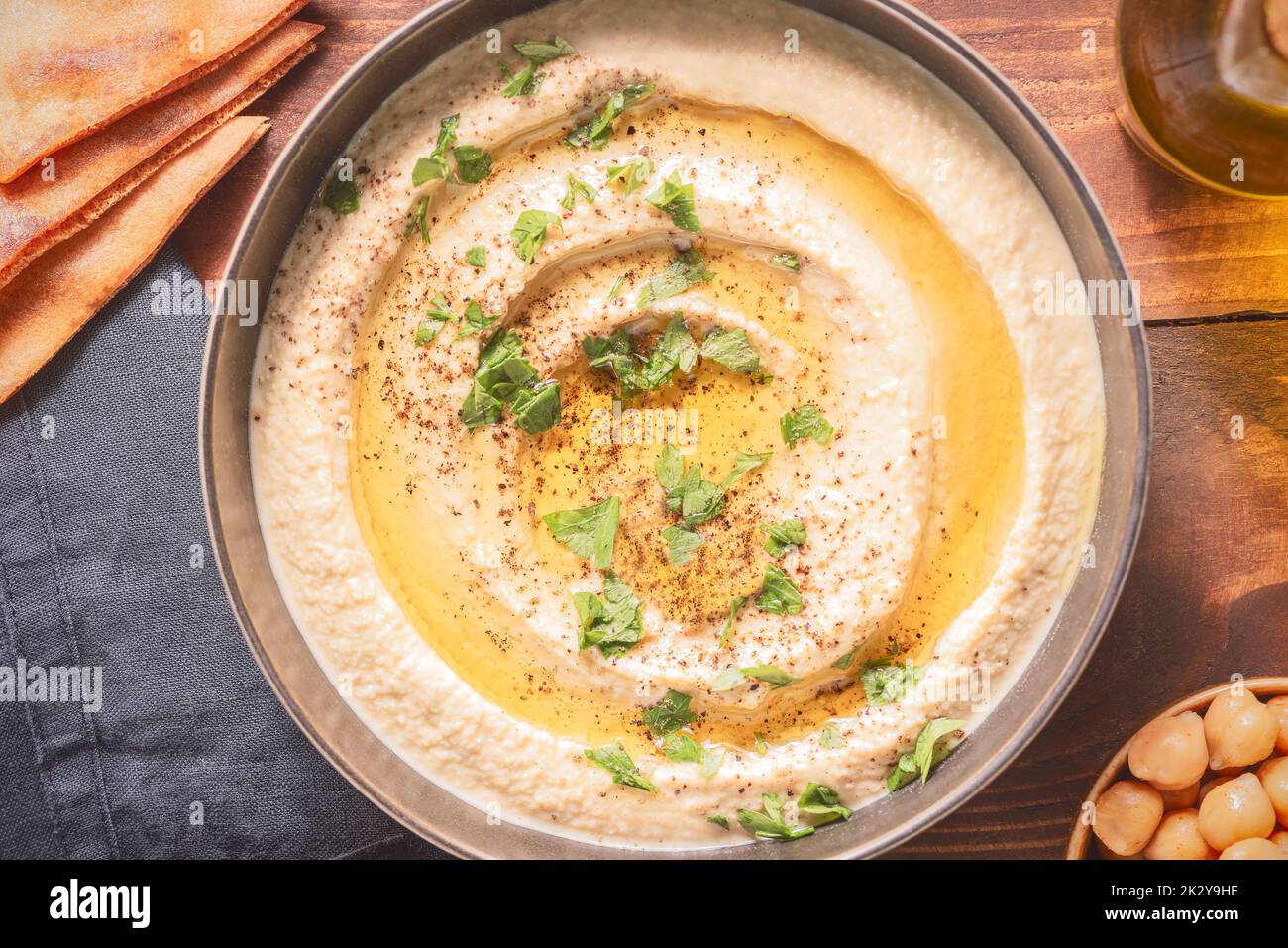 Arabische Küche; traditionelle cremige Hummus-Dip in dunkler Schüssel. Garniert mit Olivenöl, Paprika und Petersilie. Draufsicht mit Nahaufnahme. Stockfoto