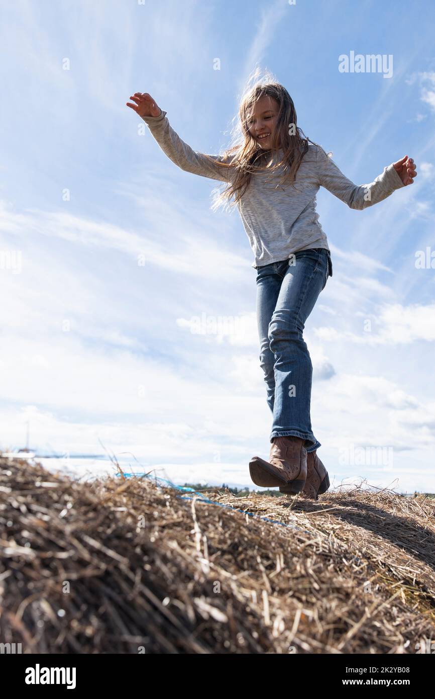 Glückliches Mädchen in Cowboystiefeln, das auf sonnigen Bauernhofballen spielt Stockfoto