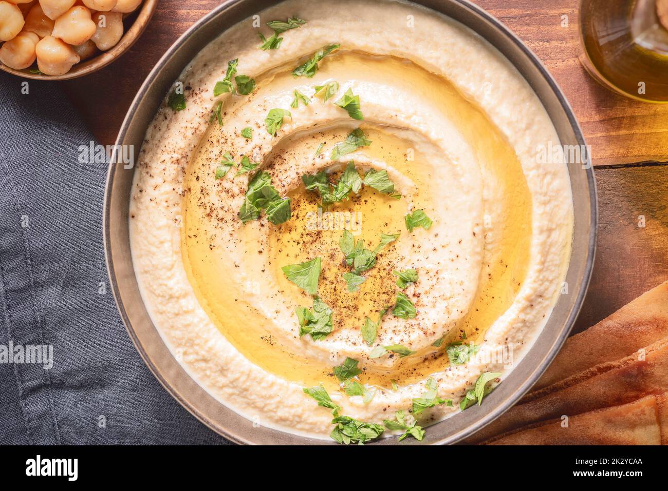 Arabische Küche; traditionelle cremige Hummus-Dip in dunkler Schüssel. Garniert mit Olivenöl, Paprika und Petersilie. Draufsicht mit Nahaufnahme. Stockfoto