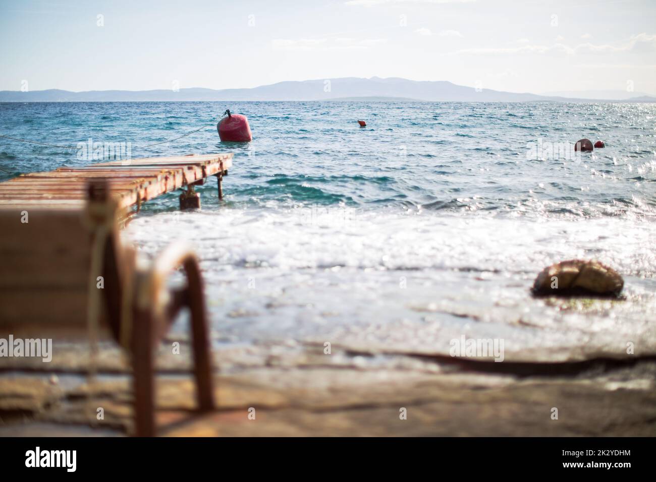 Eine selektive Fokusaufnahme eines Strands mit einem hölzernen Dock und des Meeres mit schwimmenden Geräten Stockfoto