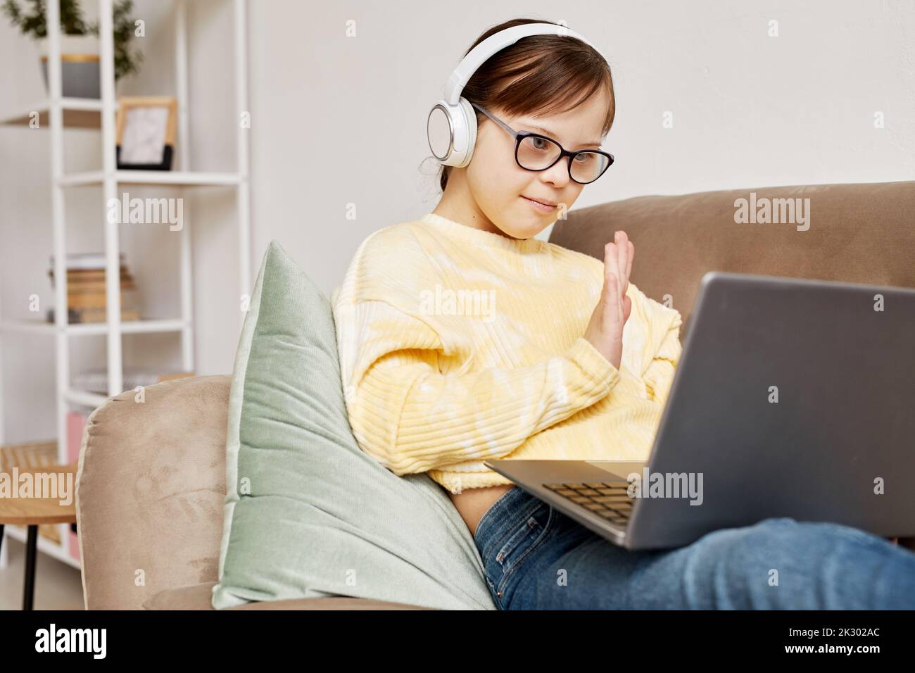Portrait eines Teenagers mit Down-Syndrom, das bei der Kamera winkt im Online-Unterricht Stockfoto