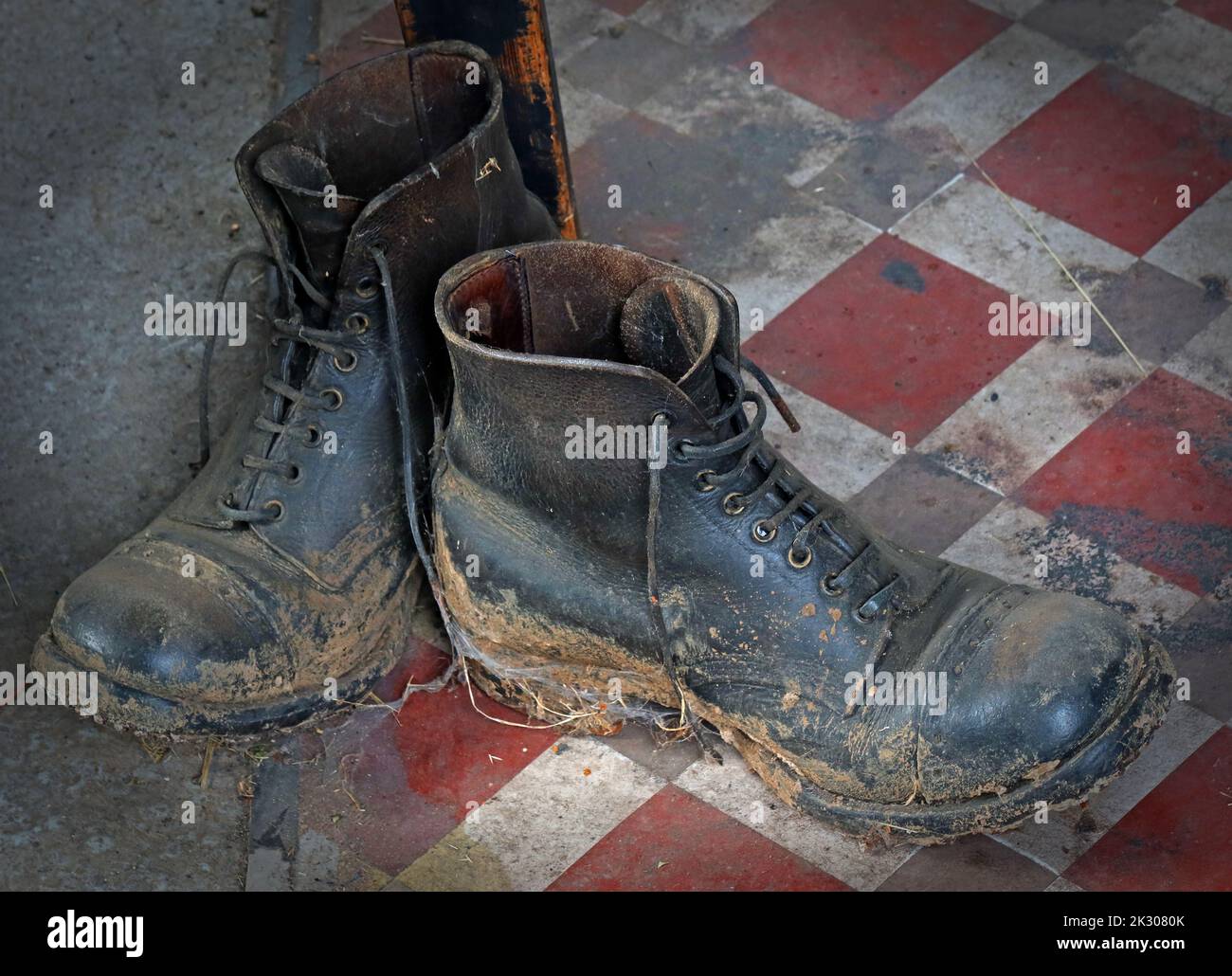 Schlammige Arbeitsstiefel aus Leder, auf Keramikfliesen Stockfoto