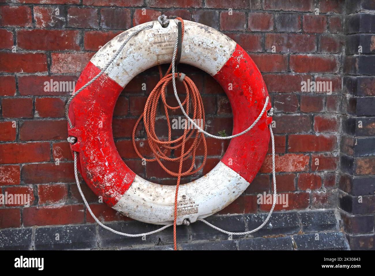Notfall Rot und Weiß, Ferryboje-Rettungsring, Sicherheitsgurt, befestigt an einer Ziegelwand neben dem Bridgewater Kanal, mit Seil Stockfoto