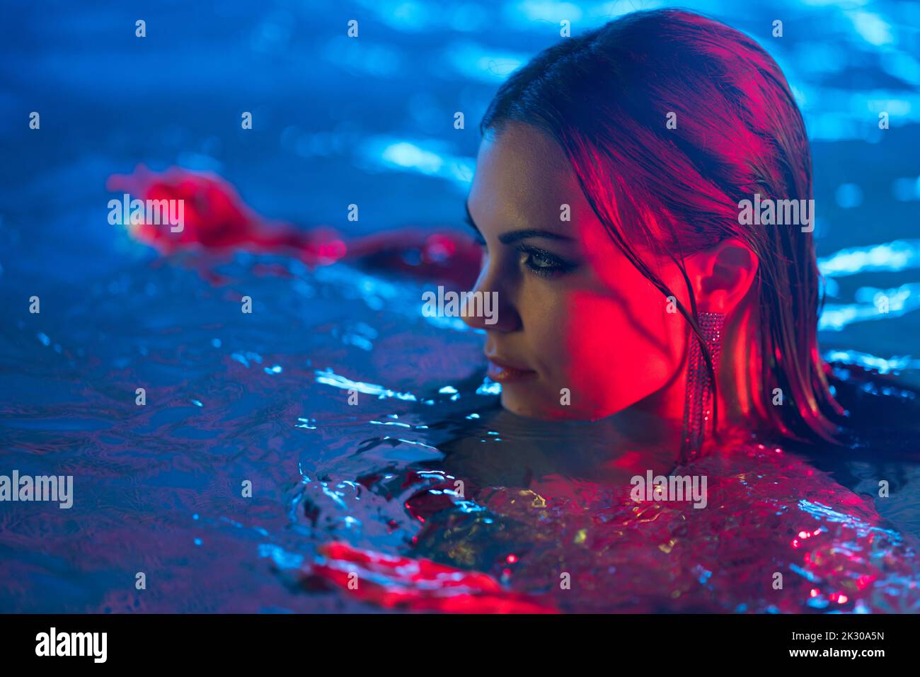 Sexy gefährliche Frau im Schwimmbad Wasser unter Neon buntes Licht. Party im Club, attraktiv chic in Pailletten Kleid genießen die Nacht Zeit. Reich Stockfoto