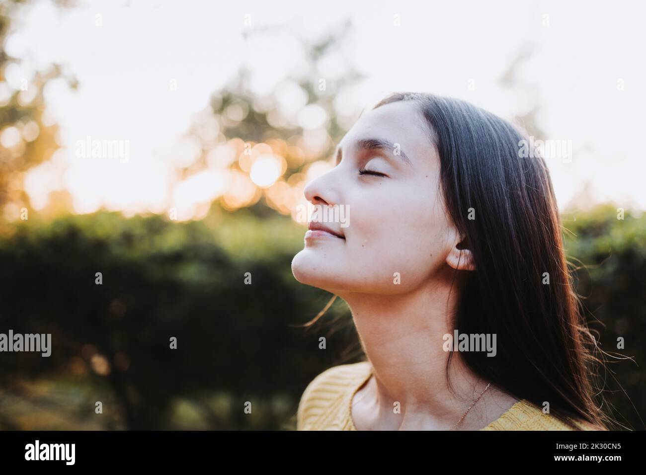 Nahaufnahme eines ruhigen Teenager-Mädchens mit geschlossenen Augen, das bei Sonnenuntergang im Park mit der Natur verbunden ist. Mentale Heilung Stockfoto