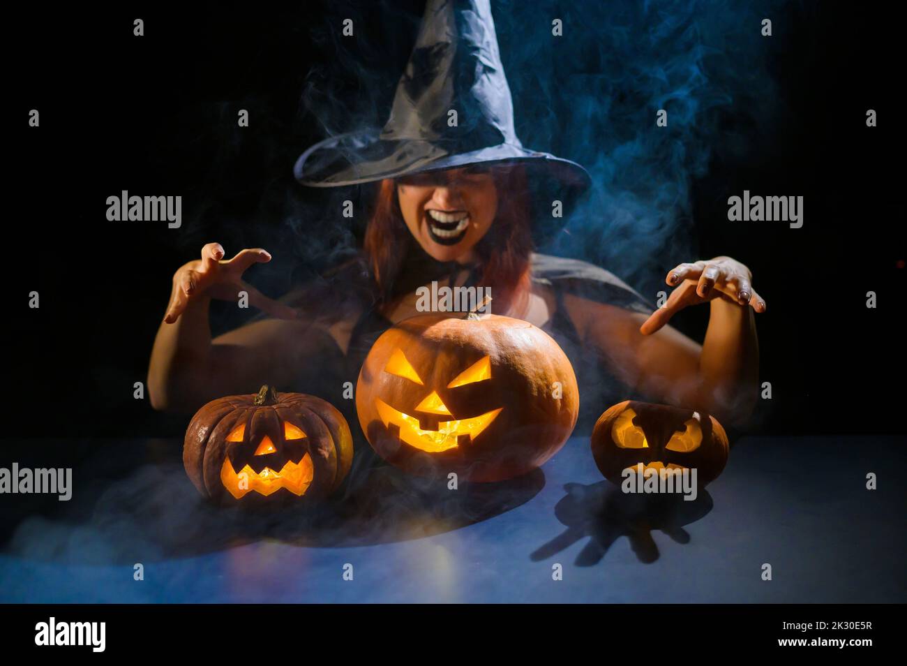 Eine ominöse Hexe im Hut zaubert über eine Jack-o-Laterne. Traditionelle halloween-Figuren 