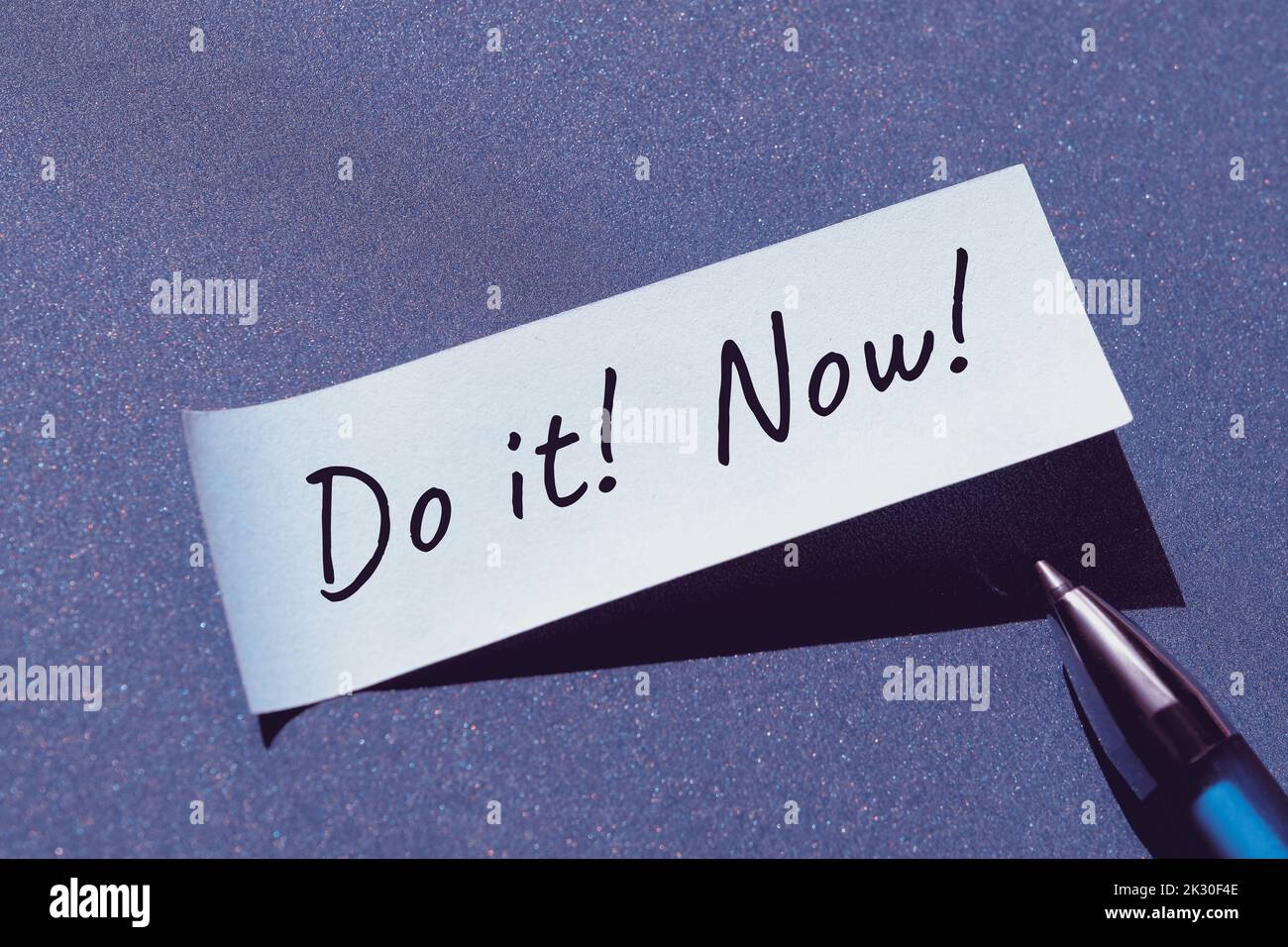 Tun Sie es jetzt Motivator Nachricht auf klebrigem Papier geschrieben, Büro Aufkleber mit Stift. Einzelner, einfacher, minimaler Motivationsnotiz-Stiker auf blauem Papierhintergrund. Stockfoto