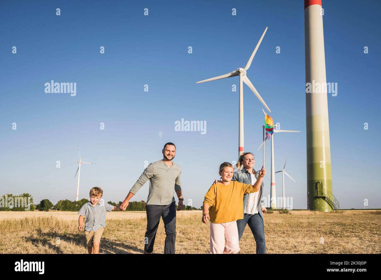 Optimistische Familie, die im Windpark läuft, Tochter, die ein buntes Windrad trägt Stockfoto