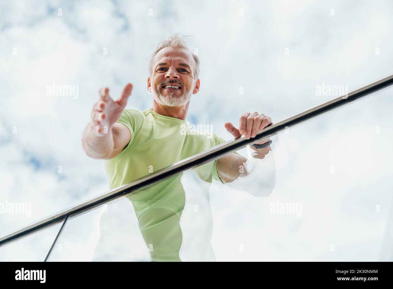 Lächelnder Mann, der am Glasgeländer steht Stockfoto