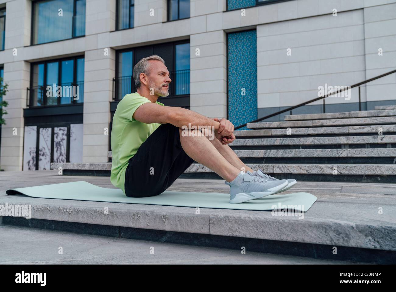 Nachdenklicher Mann, der Schritt für Schritt auf einer Yogamatte sitzt Stockfoto